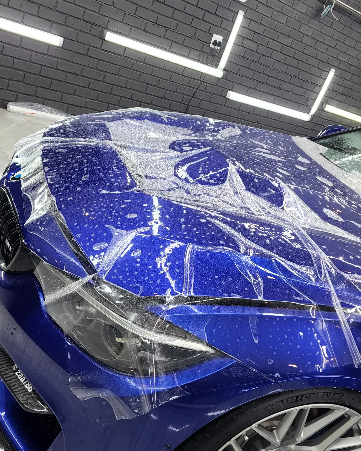 Clear film being fitted to a blue BMW bonnet at Auto Spa
